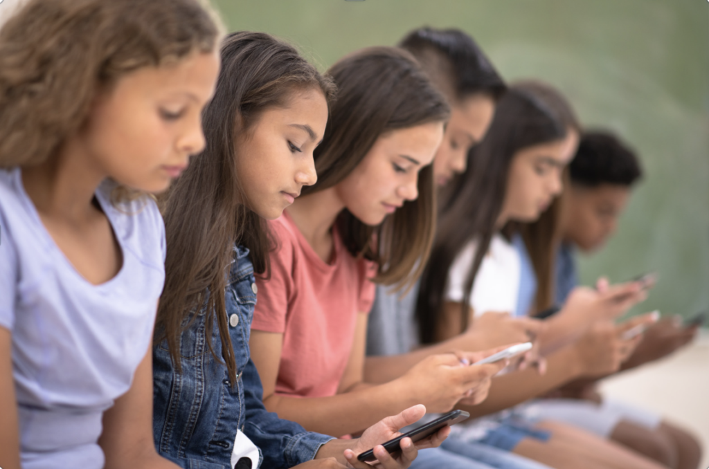 A row of children sitting, all looking at their cell phones 